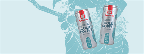 Two cans of John Wayne Cold Coffee on a light blue background with coffee bean graphics.